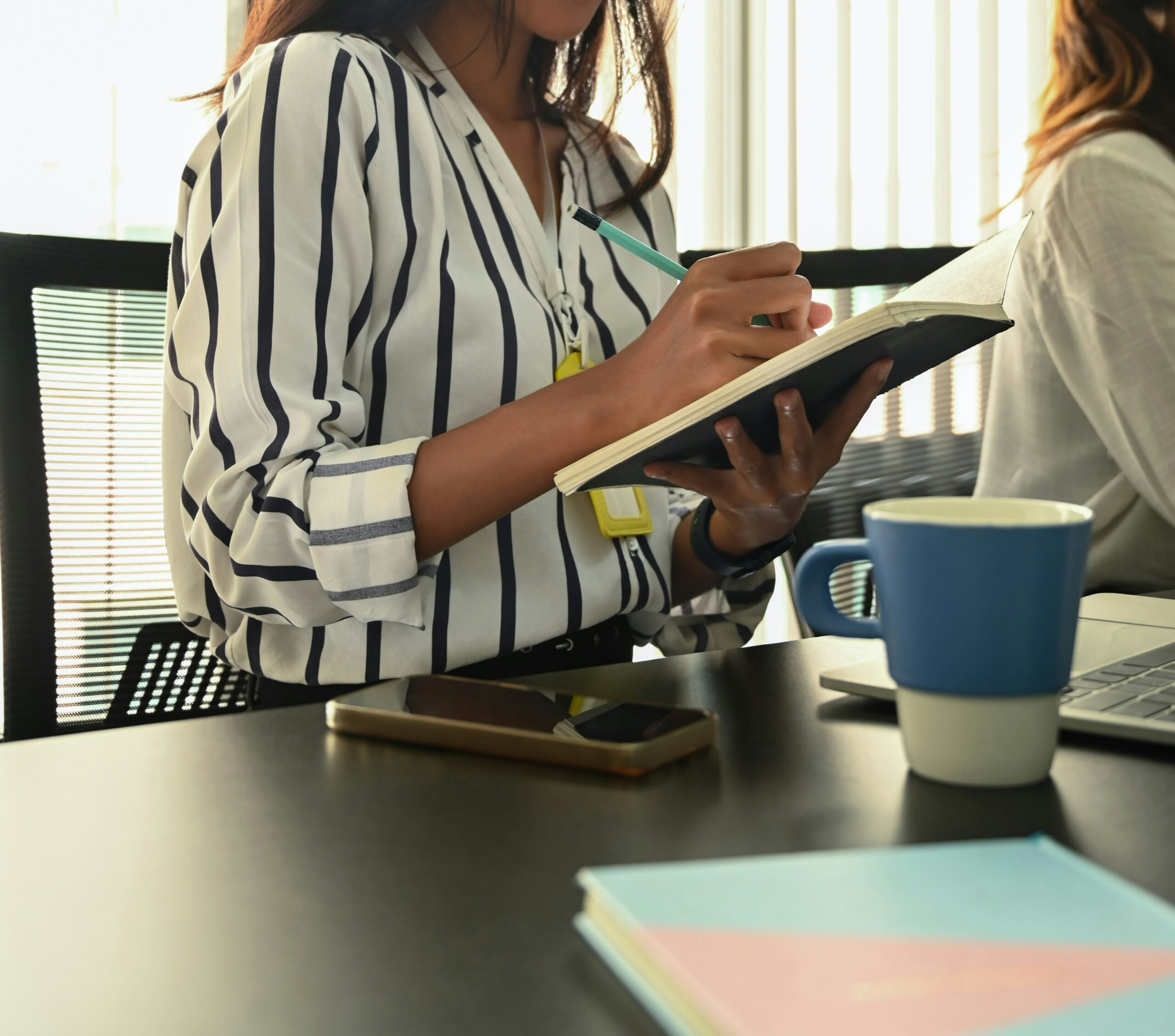 Woman writing in notebook at meeting table with coffee